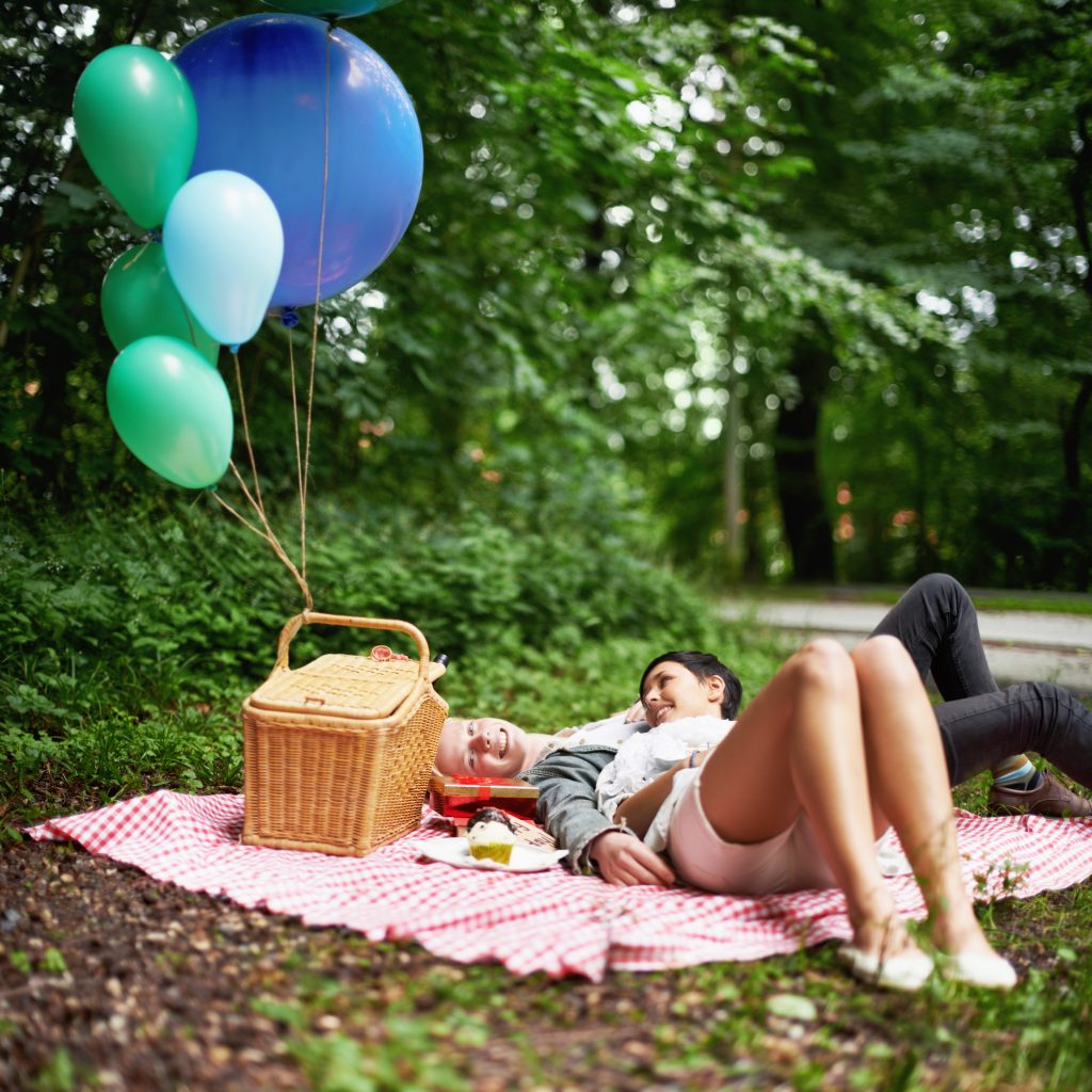 A couple lying on a blanket with balloons and a picnic basket talking about their feelings